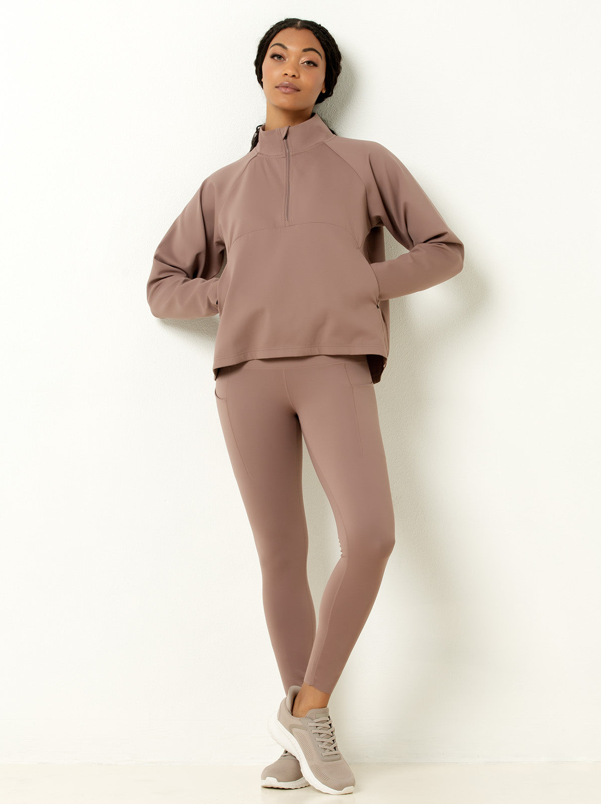 Female model posing in mauve colored jogger pants and half-zip pullover with hands in pocket.