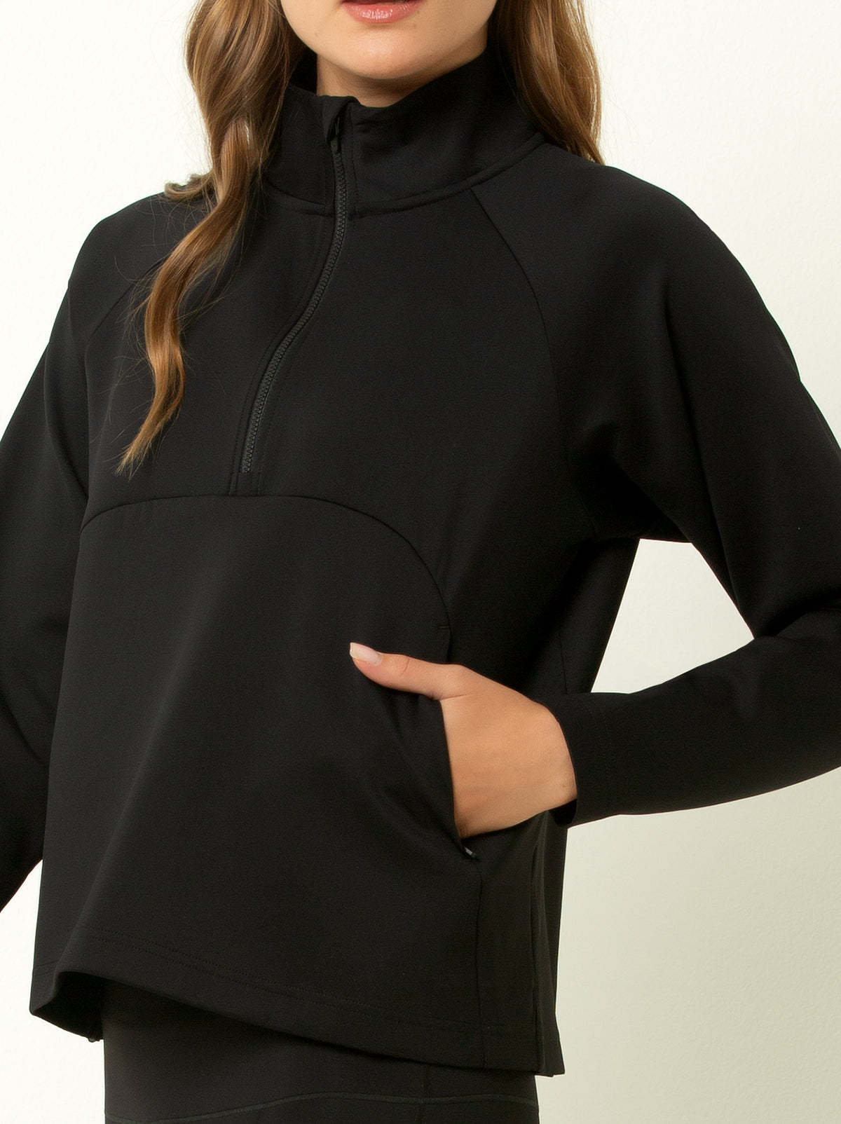 female model showing close up picture of black half zip pullover jacket with hand in pocket