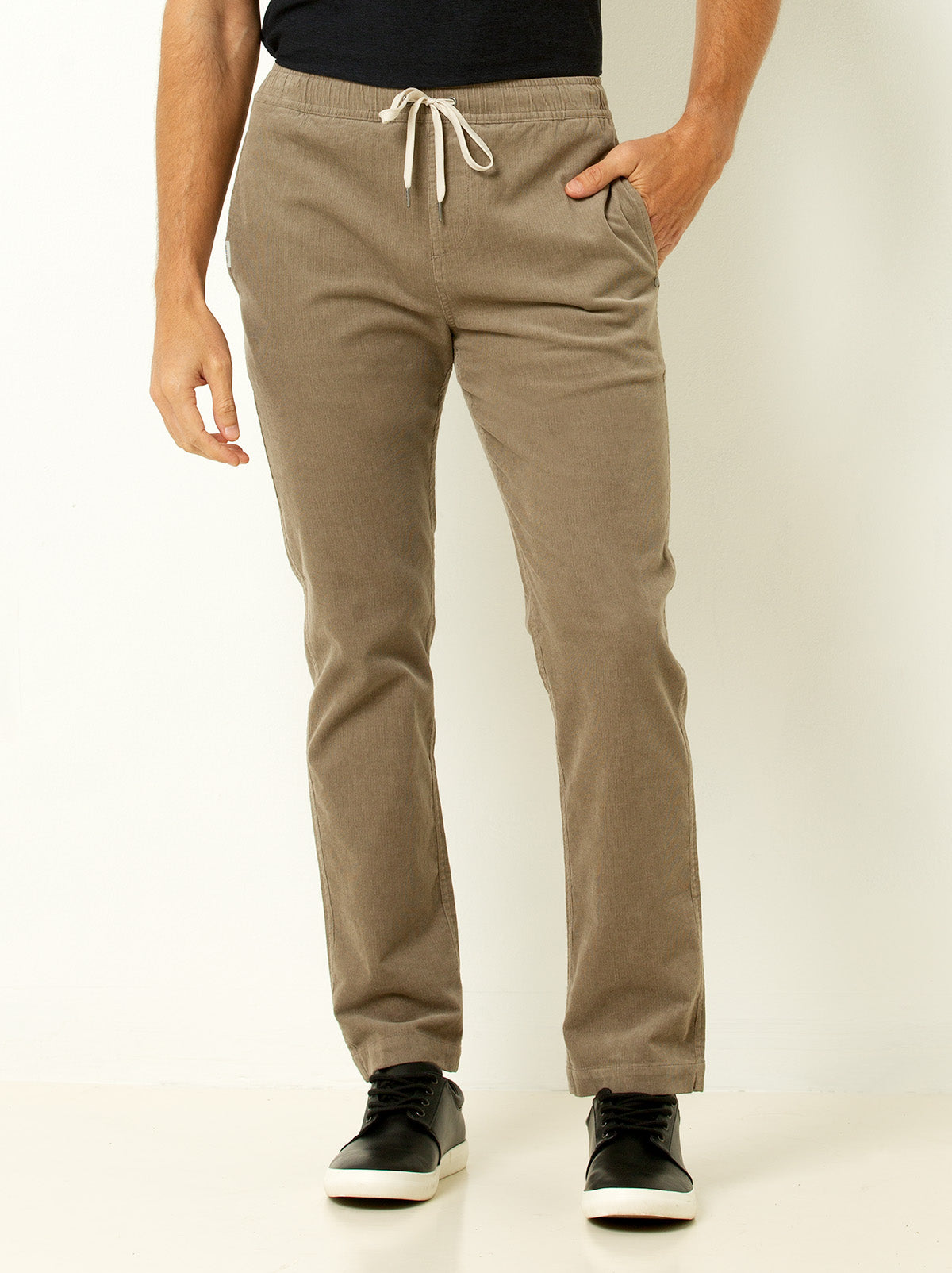 male model shown wearing beige corduroy drawstring pants from the waist down with hand in pocket