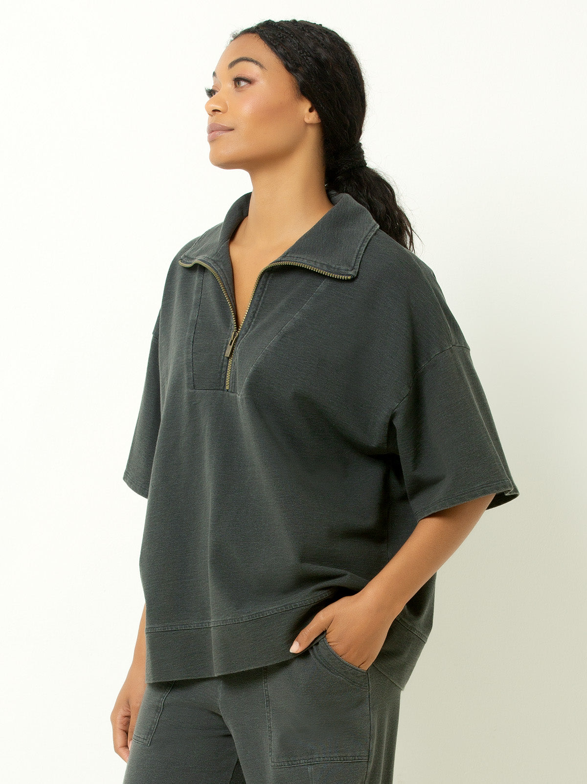 Model facing the side wearing the 1/4 zip sweatshirt with hand in pants pocket