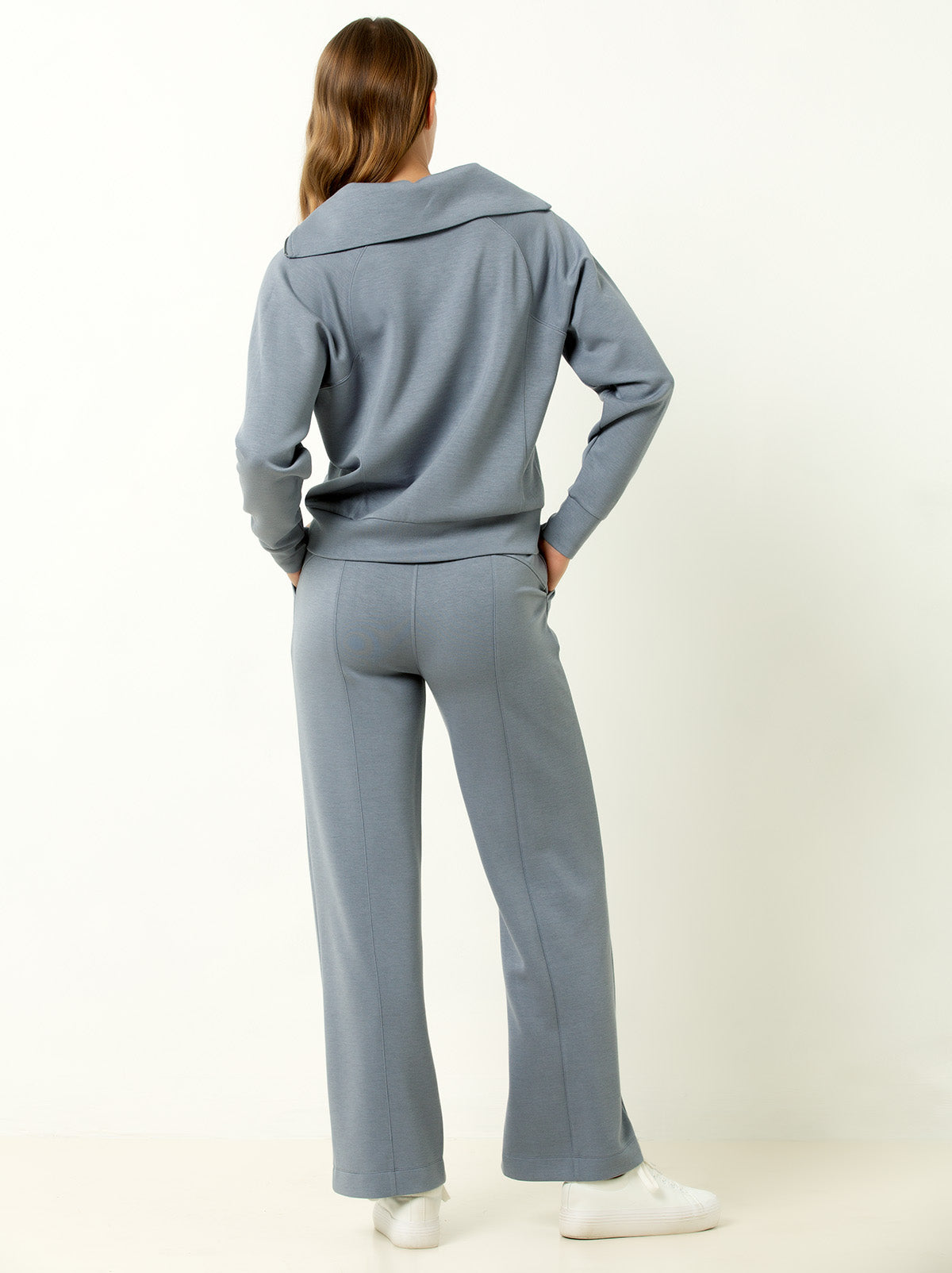 back shot of female model wearing blue gray colored jogger set with white sneakers